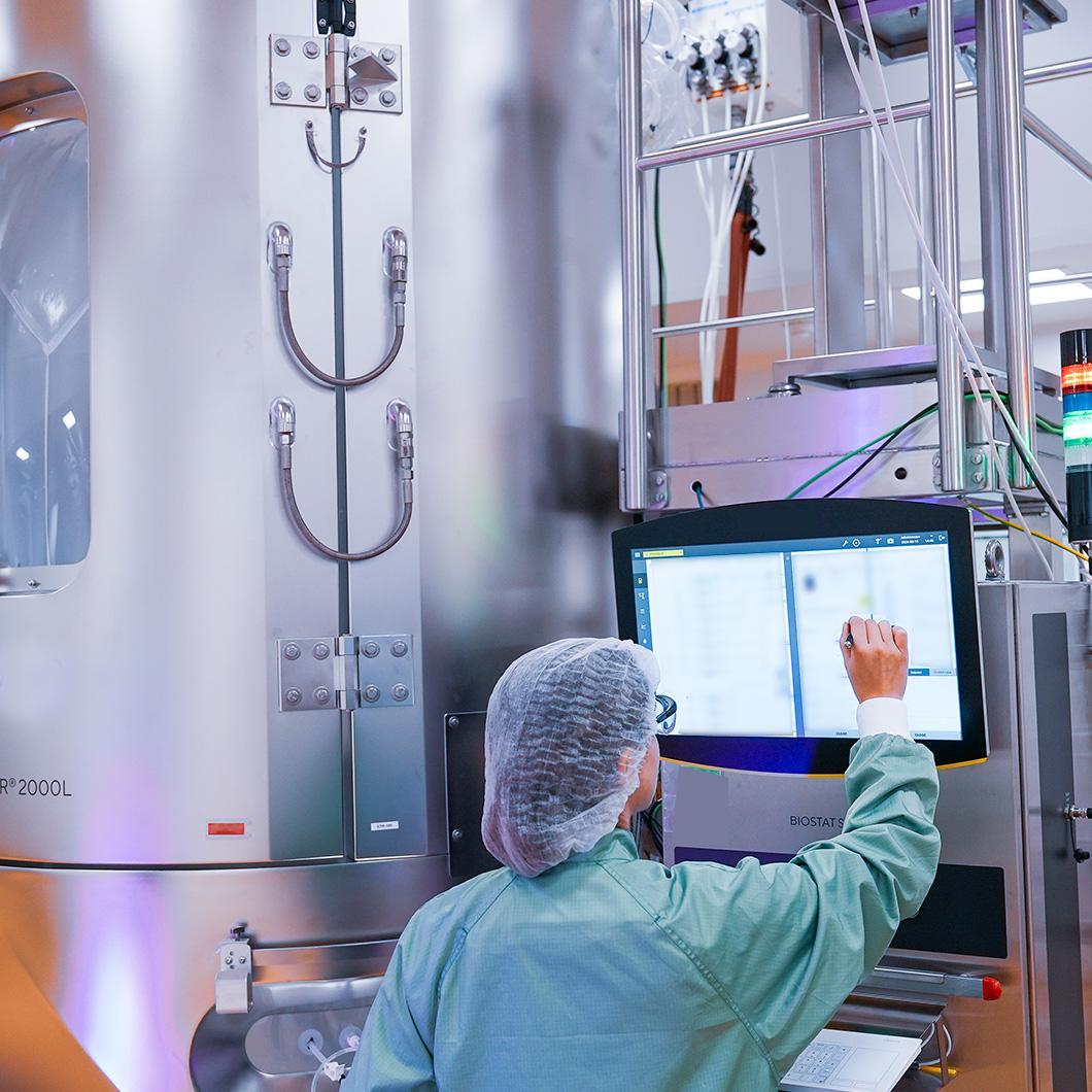 Professionnel en tenue de salle devant un équipement de laboratoire, utilisant un écran de contrôle.