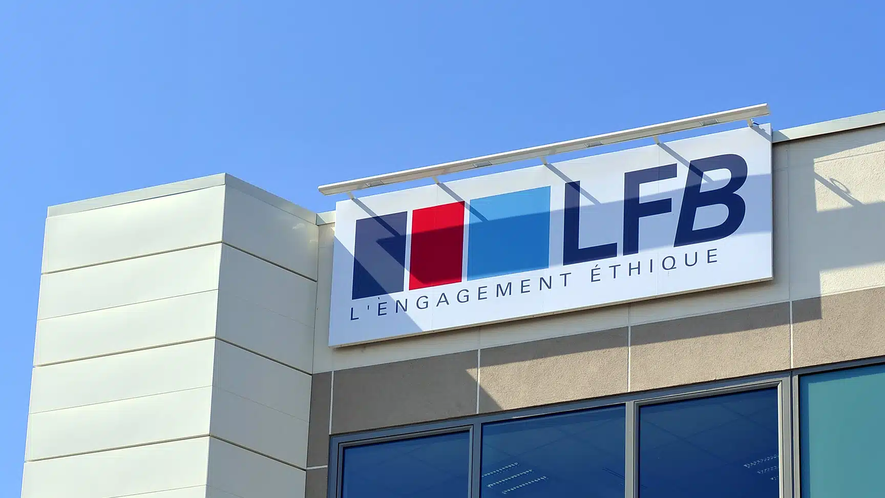 Enseigne du logo LFB « L'engagement éthique » installée en hauteur sur la façade d'un bâtiment, sous un ciel bleu dégagé.
