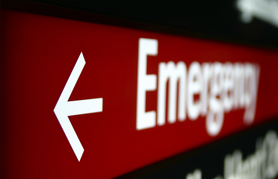Photographie en gros plan d'un panneau de signalisation rouge indiquant « Emergency » avec une flèche pointant vers la gauche.