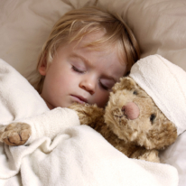 Photographie d'un jeune enfant endormi, blotti contre un ours en peluche.