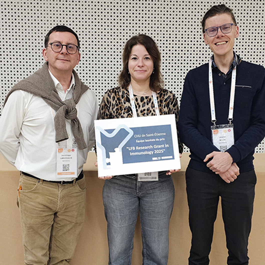 Photo de trois personnes (deux hommes, une femme) portant des badges de conférence, posant devant un mur. La femme au centre tient un panneau : « CHU de Saint-Étienne, équipe lauréate du prix "LFB Research Grant in Immunology 2025" ».