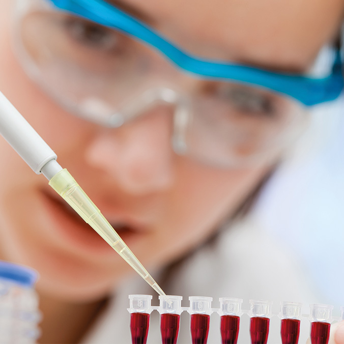 Une technicienne de laboratoire portant des lunettes de protection prélève un échantillon à la pipette dans une série de tubes