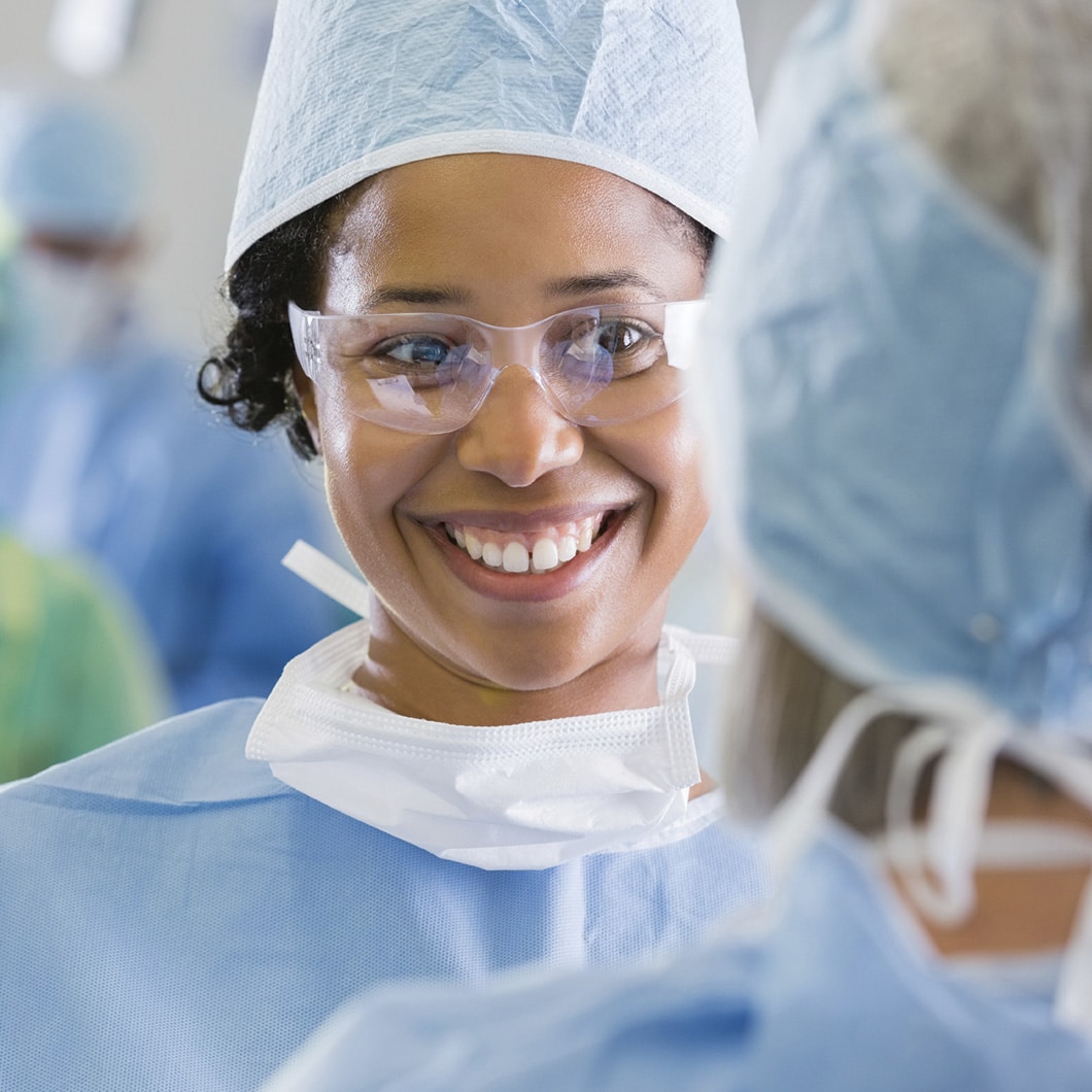 Femme en tenue de bloc opératoire souriant, entourée d'une équipe médicale.