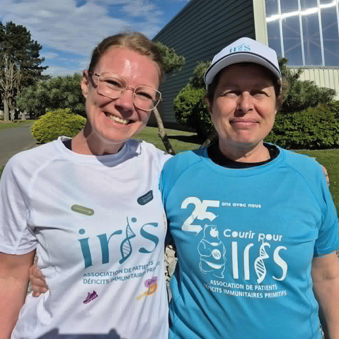 Deux femmes souriantes posent bras dessus bras dessous en extérieur, portant des t-shirts de l'association Iris, dont un marquant les 25 ans de l'opération « Courir pour Iris ».